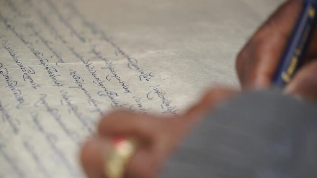 Tibetan astrologer elegantly writing on high-quality paper with a pen, focusing on creating beautiful, cursive text close-up
