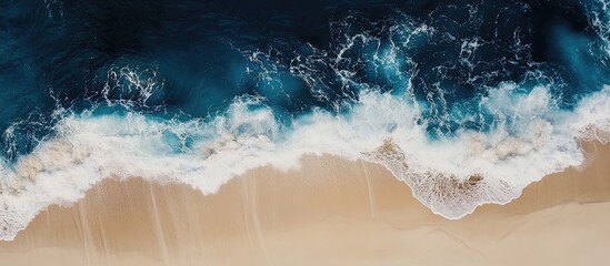 Fototapeta premium Aerial view of ocean waves crashing onto a serene sandy beach creating foamy patterns and tranquil coastal scenery