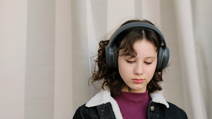 A girl with headphones enjoys a quiet moment, her expression calm and reflective. The photo...
