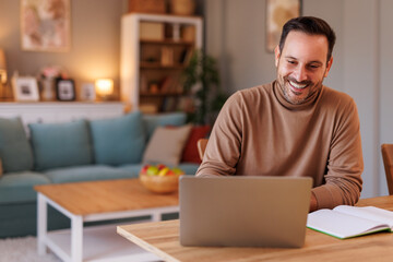 Portrait of handsome entrepreneur checking e-mails over laptop while sitting at desk in home office