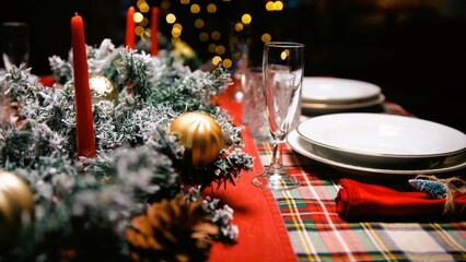 A picture-perfect Christmas dinner table. Front view photo of plates, cutlery, balls, napkin, candles, snowman, confetti, spruce twigs on beige background with advert area.Defocused christmas tree.
