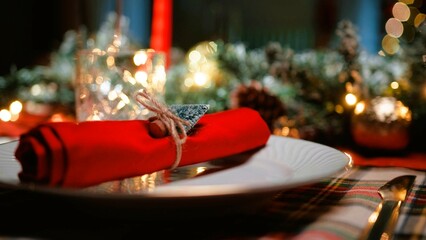 A picture-perfect Christmas dinner table. Front view photo of plates, cutlery, balls, napkin, candles, snowman, confetti, spruce twigs on beige background with advert area.Defocused christmas tree.
