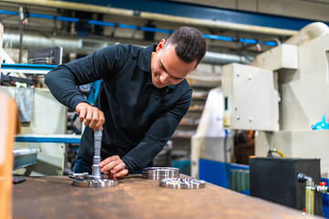 Man measuring metal pieces using micrometer at factory