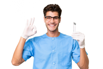 Young dentist man holding tools over isolated background showing ok sign with fingers