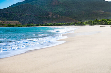 A beautiful beach with a clear blue ocean and a few boats in the water