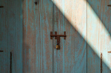 closed blue vintage wooden door or close old peeling cyan paint wood window wall to rusty iron door latch lock with contrast sunlight for home retro decor and architecture interior exterior background