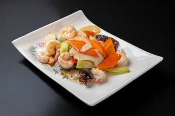 Crispy shrimp stir-fried with vegetables in a white dish on a dark background, an Asian cuisine dish