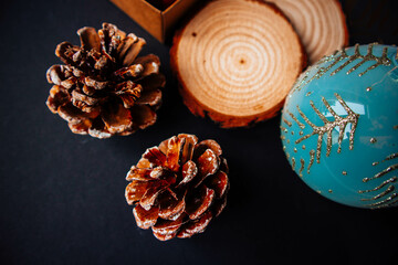 A box with red Christmas tree decorations with wooden stands, pine cones, New Year's packaging and a New Year's toy on a black paper background.
