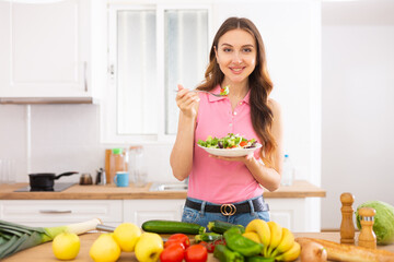 Slim young woman eating vegetable salad in home kitchen