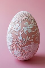 Fototapeta premium Easter egg displays an elegant lace overlay pattern in white, with detailed bees and flowers on a pink background