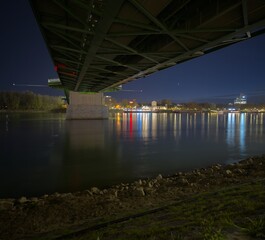 A unique nighttime perspective captured beneath a brightly illuminated bridge, with colorful...