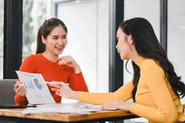 Obraz premium Two women discussing business report with charts and graphs, showcasing teamwork and collaboration in modern office setting