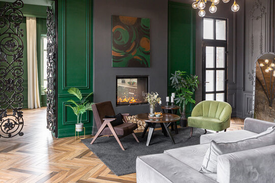 the dark brutal interior of the living room in a historical style in a mansion with panoramic windows. grey-green walls, brown parquet and modern furniture.