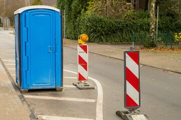 Mobile toilet placed on street during roadworks with warning signs