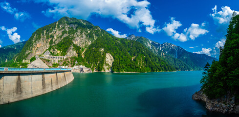 Panorama Beautiful scenery of Kurobe Dam on a brisk, with colorful lakeside mountains and crystal clear lake water under blue sunny sky in Tateyama Kurobe Alpine Route, Toyama, Japan