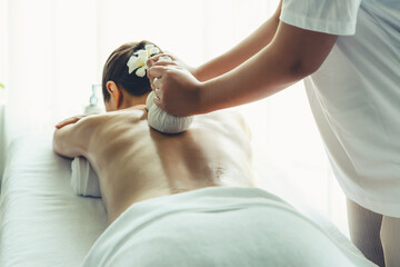 Hot herbal ball spa massage body treatment, masseur gently compresses herb bag on woman body....
