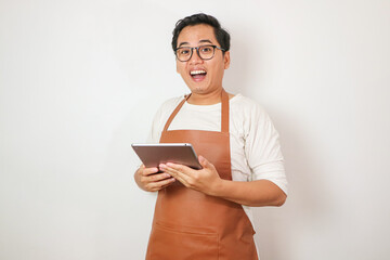 Asian grocery store manager salesman in apron using digital tablet counting goods in supermarket. Male worker employee doing inspection of products regular inventory to control goods online order