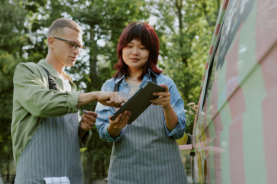 Low angle shot of biracial food truck workers discussing menu while looking at it on tablet