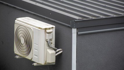 A rusty air conditioning unit affixed to a modern building exterior highlights energy efficiency...