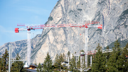 Red and white construction cranes tower against a mountainous backdrop, symbolizing industrial...