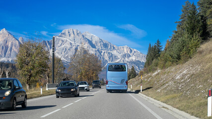 A serene mountain road with vehicles, including a tour bus, captures the essence of scenic travel...