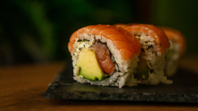 Close-up of sushi with salmon, avocado and cream cheese on a black board with a green background