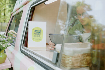 Pastel pink green food truck with male Caucasian worker using tablet parked in local park