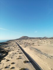Aerial view of a coastal road through the sand dunes with sea views and blue sky background. Taken in Fuerteventura. 
