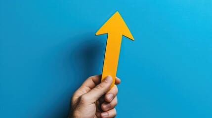 A male hand holding a bright yellow arrow on a blue background.