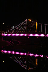 Obraz premium bridge illuminated with pink lights at night, reflecting on the calm water below. The image evokes a sense of tranquility and beauty.