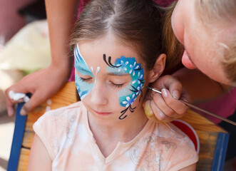 Child animator, artist's hand draws face painting to little girl. Child with funny face painting....