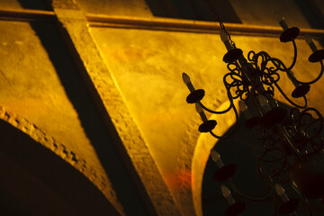 Elegant chandelier casting warm light against an intricately designed wall in an historic building...
