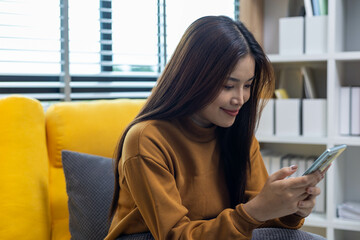 A young woman is playing with her mobile phone and wearing earphones on a sofa in a living room