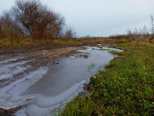 Beautiful natural autumn landscape in the fields with frozen water in a puddle on a field road. A...