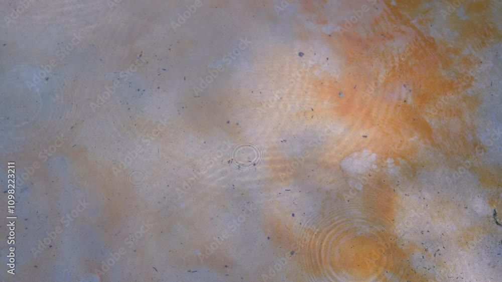 Poster Water surface with ripples and drops falling creating circles. Uneven bottom color, ranging from light to dark orange. Slow motion, high angle shot.