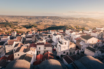 Ancient town on hill side with levels of whitewashed houses and tiled roofs at sunset, Pisticci, Italy