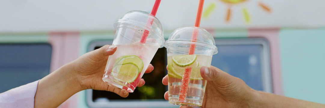 Website banner with unrecognizable couple clinking transparent plastic gups with citrus lemonade and slices of lime inside