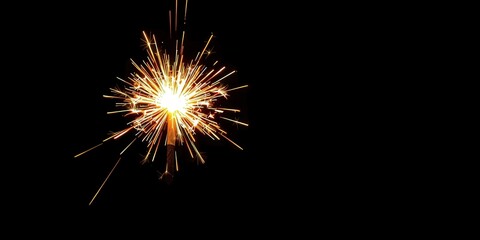 A glowing sparkler in a black background, radiating a bright yellow and orange light, creating a festive, celebratory mood