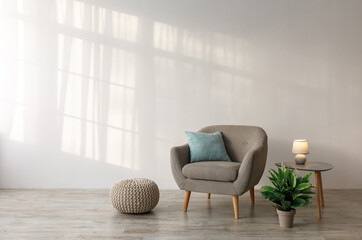 Comfortable armchair with pillow, luminous lamp on table, potted plant and ottoman on floor on gray...