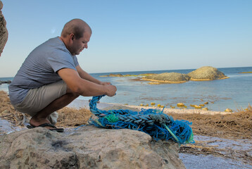 A person unbraiding a massive synthetic fishing rope on the shore of the sea