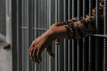 hands of a prisoner behind prison bars on black background	
