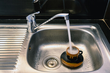 Ceramic coffee cup with sink tap hole cover in stainless steel kitchen sink. Used coffee cup with...