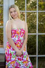 Outdoor  portrait of a beautiful  blond  young  woman in a colorful  flowered  dress  in  front  of  glass  paned  door