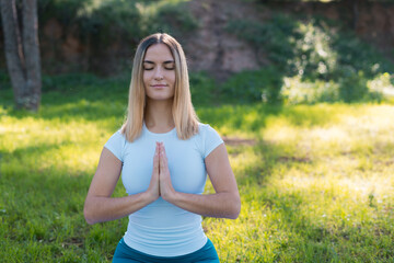 young woman sitting on yoga mat meditating in park