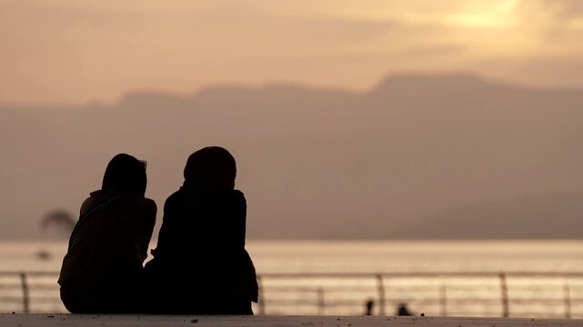 Silhouette of two Arab women in front of the sea at sunset
