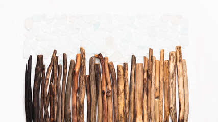 Driftwood sticks arranged in a row with scattered sea glass pieces, forming a rectangle against a clean white background, creating a harmonious and textured horizontal display of natural materials