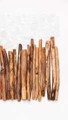 Driftwood sticks arranged in a row with scattered sea glass pieces, forming a rectangle against a clean white background, creating a harmonious and textured vertical display of natural materials