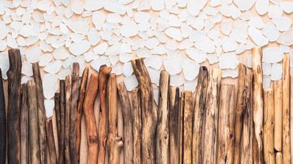 A row of driftwood sticks arranged in a gradient from dark to light on a beige background, with scattered sea glass pieces, highlighting natural textures and balanced simplicity in design