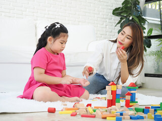 Naklejka premium Autistic girl playing building wooden blocks with her mother.