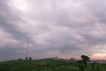 sky with thick, gray clouds looms over a green field. A lone tower stands tall, adding a touch of human presence to the vast landscape.